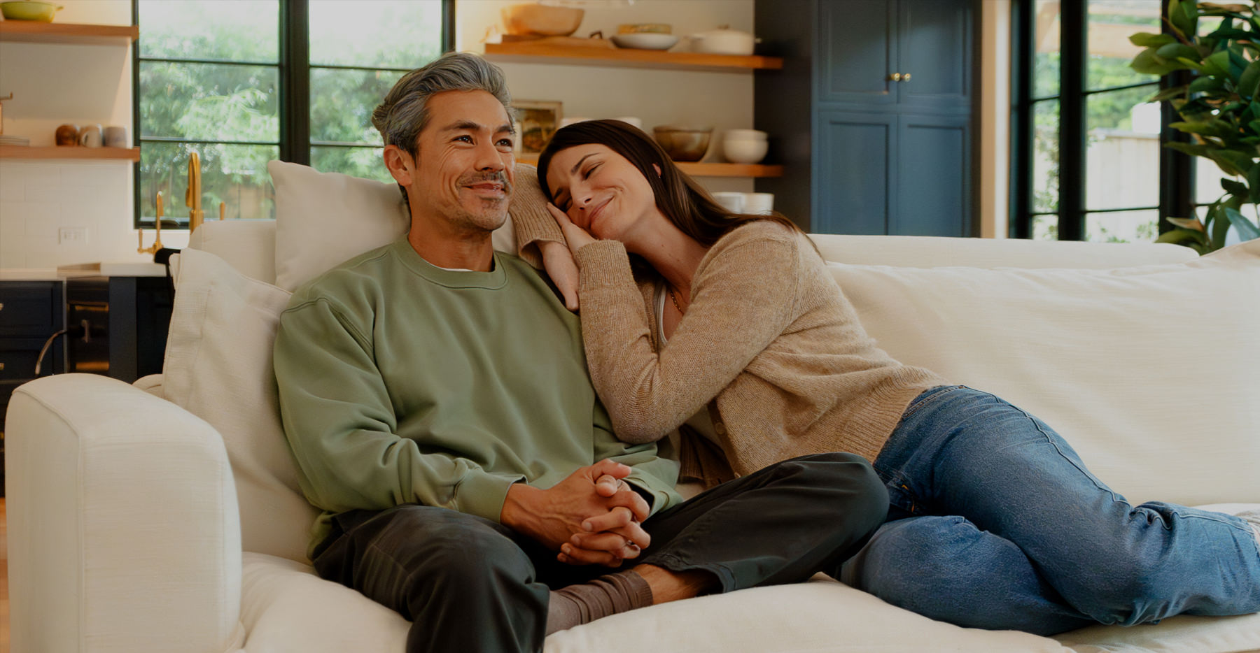 A smiling couple relaxing together on a comfortable, white sofa in a warmly lit living room
