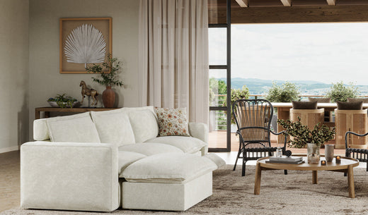 A bright, coastal-inspired living space featuring a comfortable white sectional sofa that opens to an outdoor terrace or balcony.