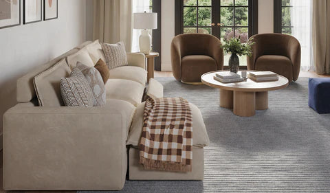 A stylish living room featuring a three-seat chaise sofa with decorative pillows, complemented by two modern armchairs.